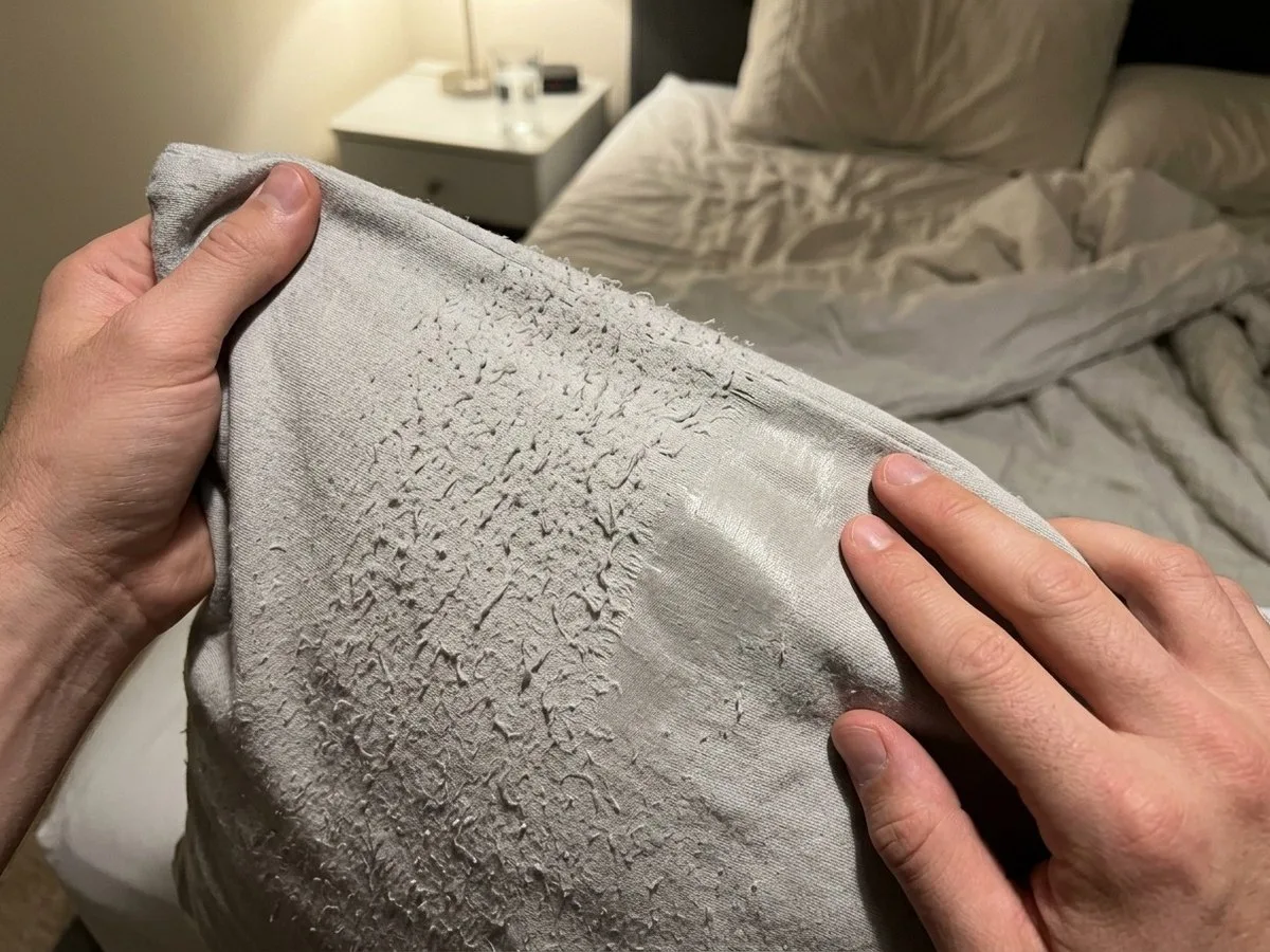 Pregnant woman sitting up in bed at night under a lamp, running her hand over a pilled, worn patch on a grey pillow cover