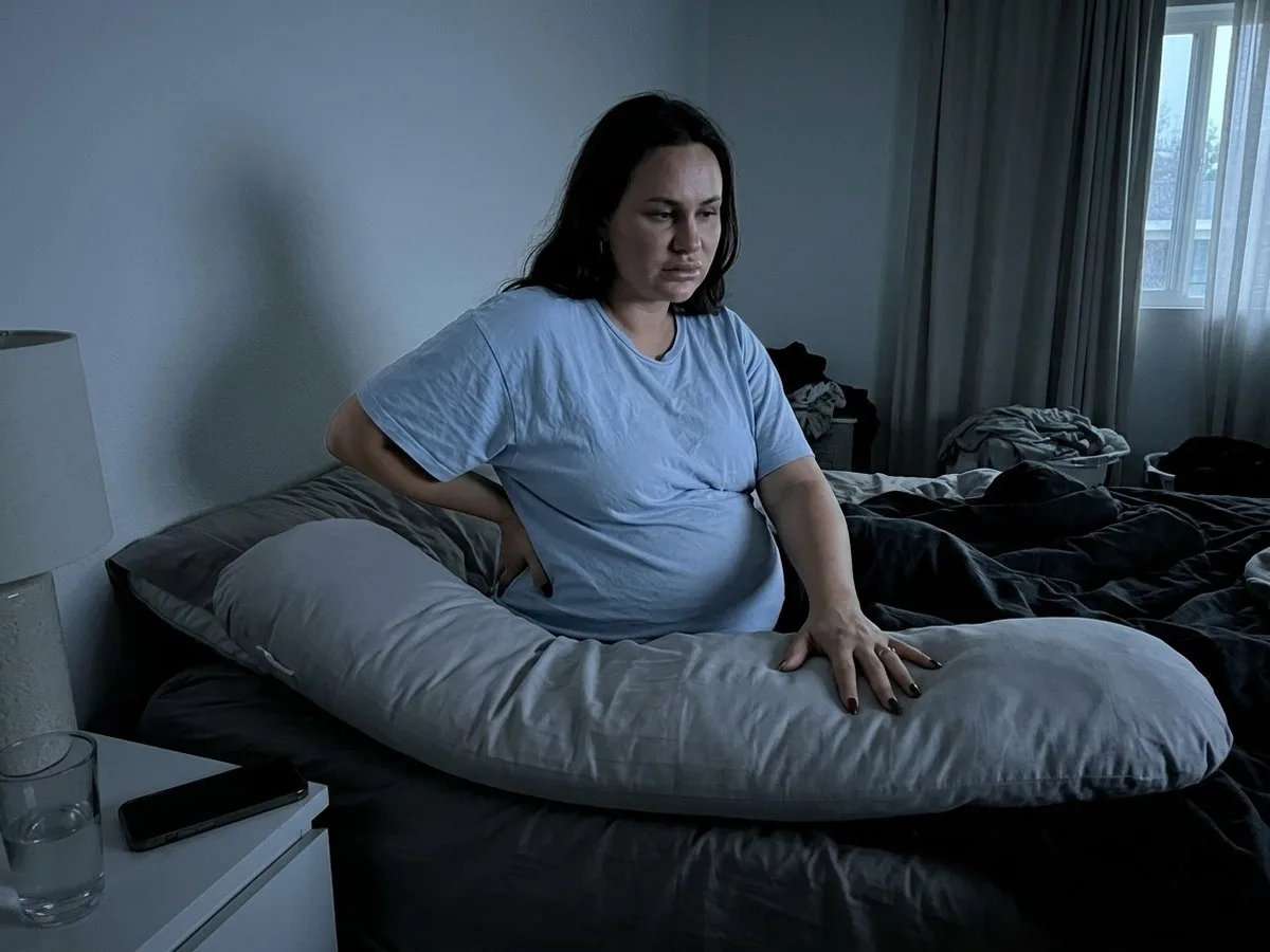 Pregnant woman sitting up in bed before dawn pressing her hand into a flattened section of her pregnancy pillow