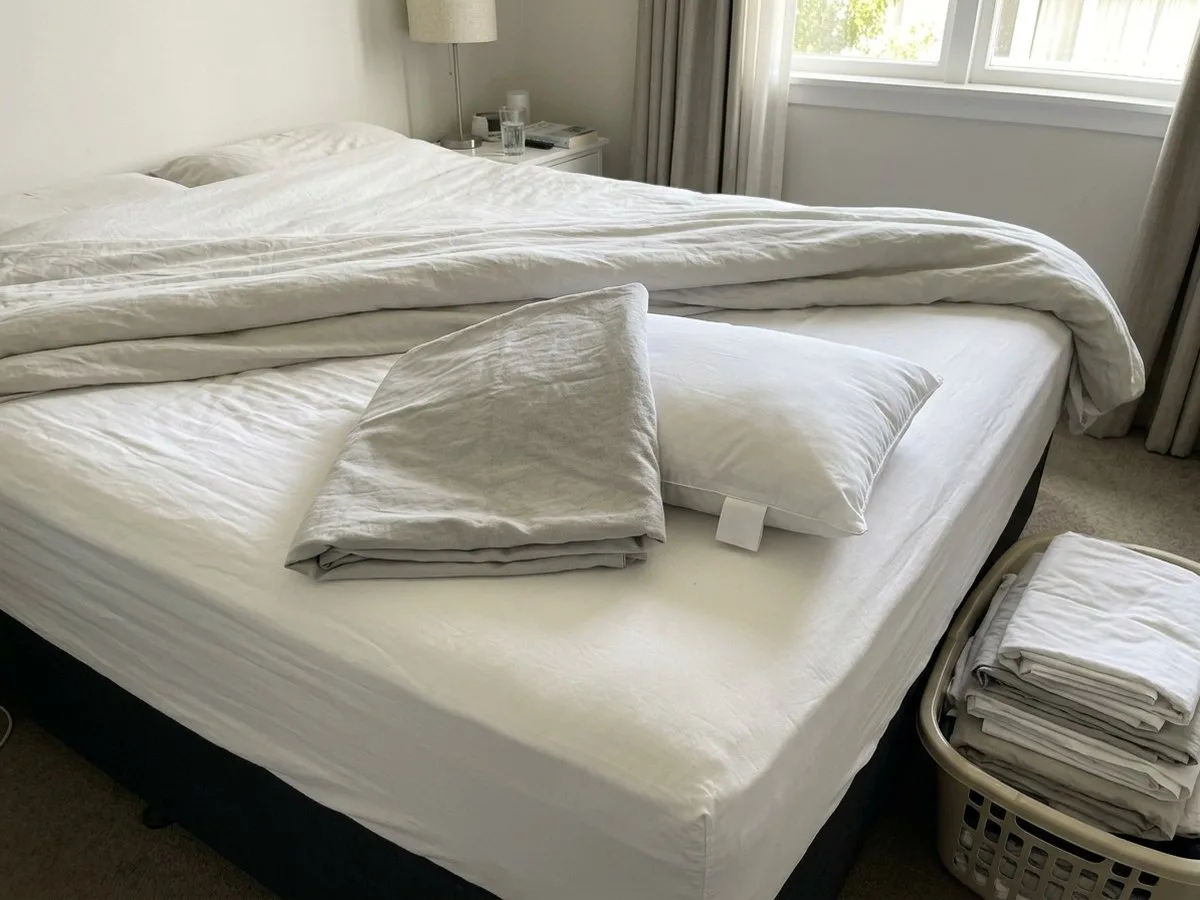 Pregnant woman sitting on her bed in daylight, reading a reply on her phone, a pillow cover folded beside her and the inner pillow next to it