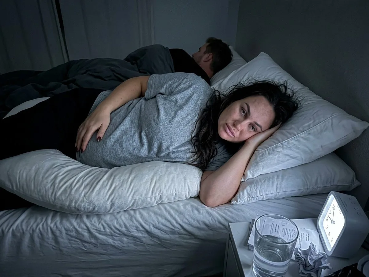 Exhausted pregnant woman awake at night inside a flattened oversized U pillow with two regular pillows piled on top