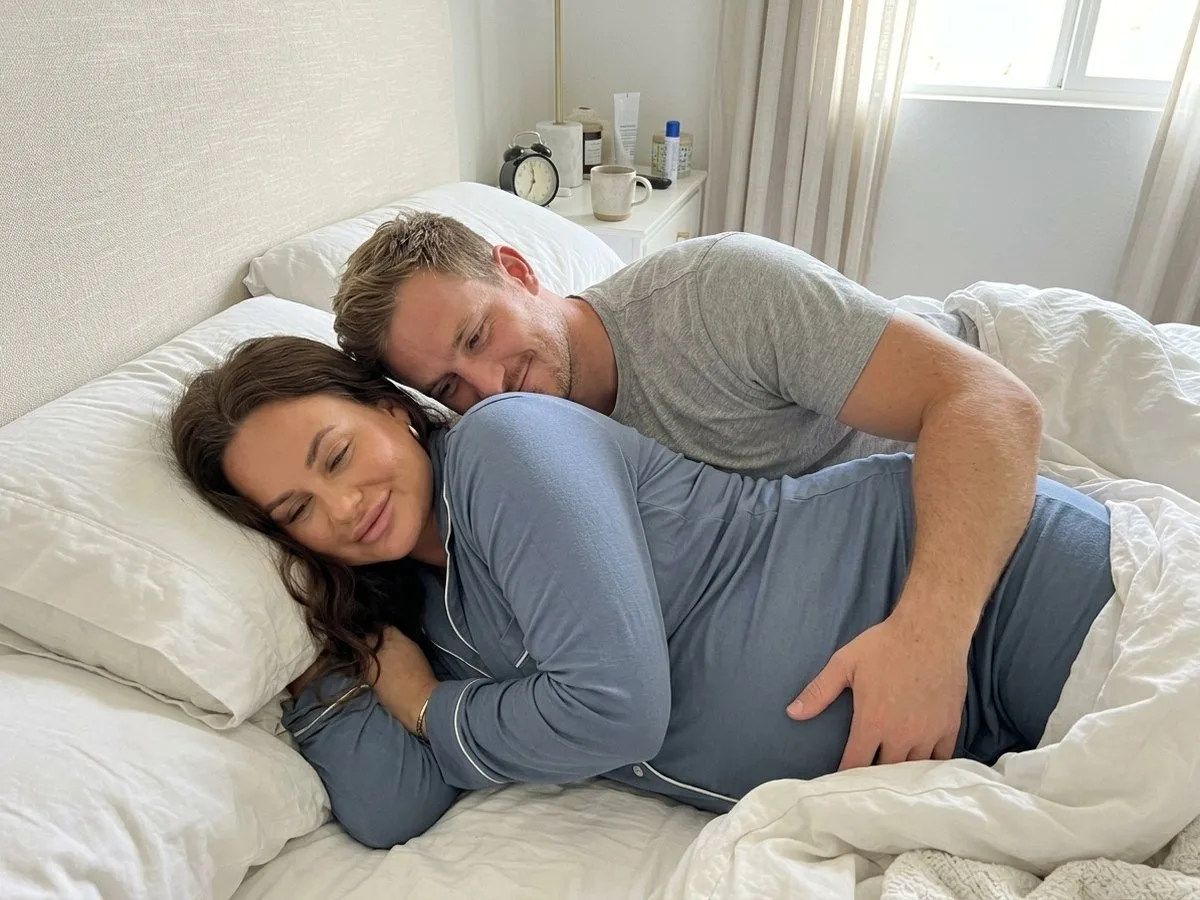 Early sunny morning, pregnant woman waking up rested on her side with her partner's arm still around her from behind