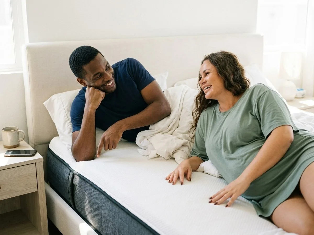 Sunny Sunday morning, pregnant woman laughing in bed as her partner, still on his side of the shared queen bed, teases her