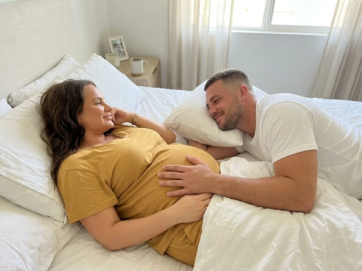 Sunday morning, partner lying close resting his hand on his pregnant partner's bump as she smiles