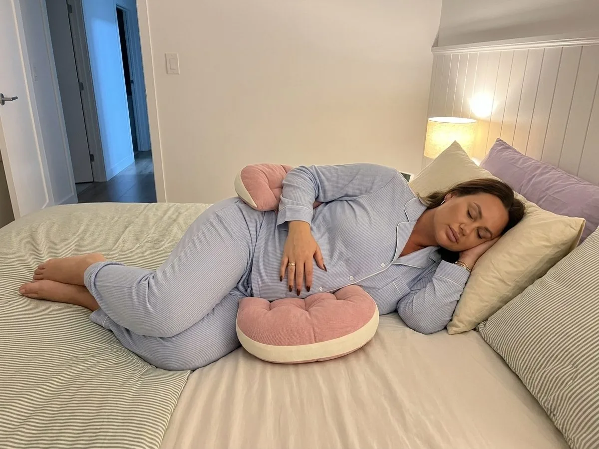 Pregnant woman sleeping on her side with one pink wedge under her bump, the other behind her lower back