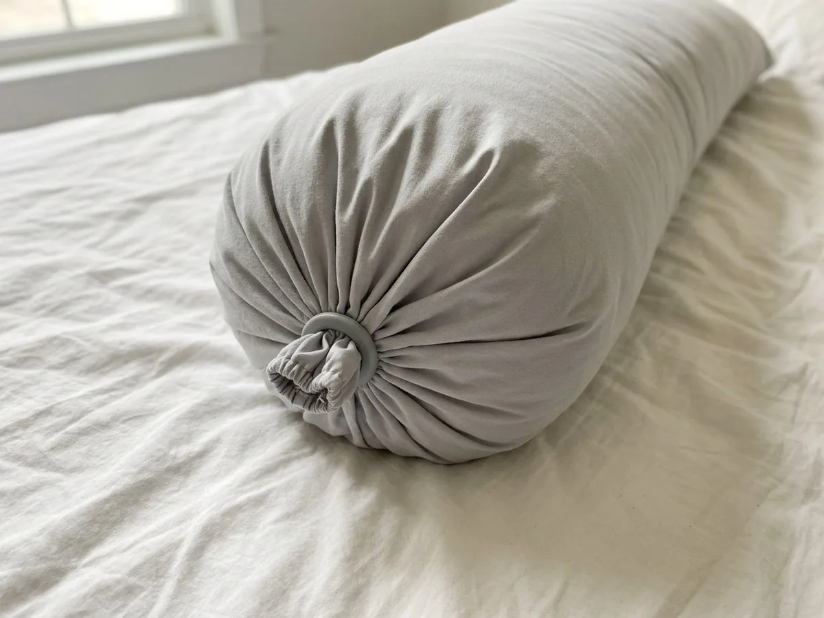 Pregnant woman awake on her side at night, pulling at a small hard ring on the end of her long pillow near her ankle